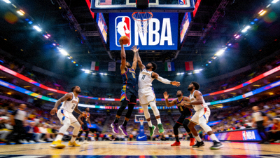 NBA篮球比赛现场，球员正在激烈对抗，背景是巨大的NBA标志